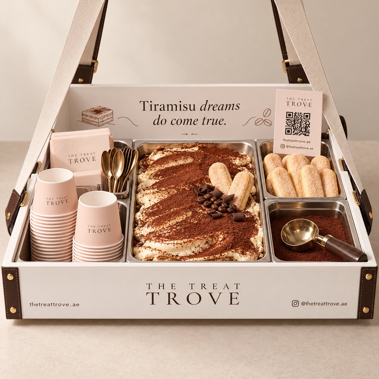 A white Treat Trove serving tray with individual portions of cocoa-dusted tiramisu, ladyfingers, blush-coloured cups and gold spoons.